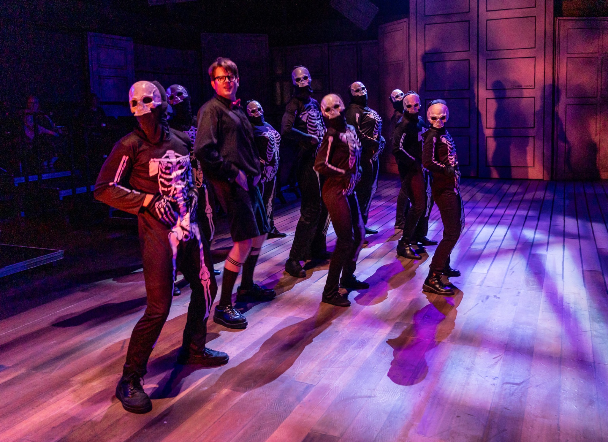 Ensemble in skeletal costumes advances under purple light.