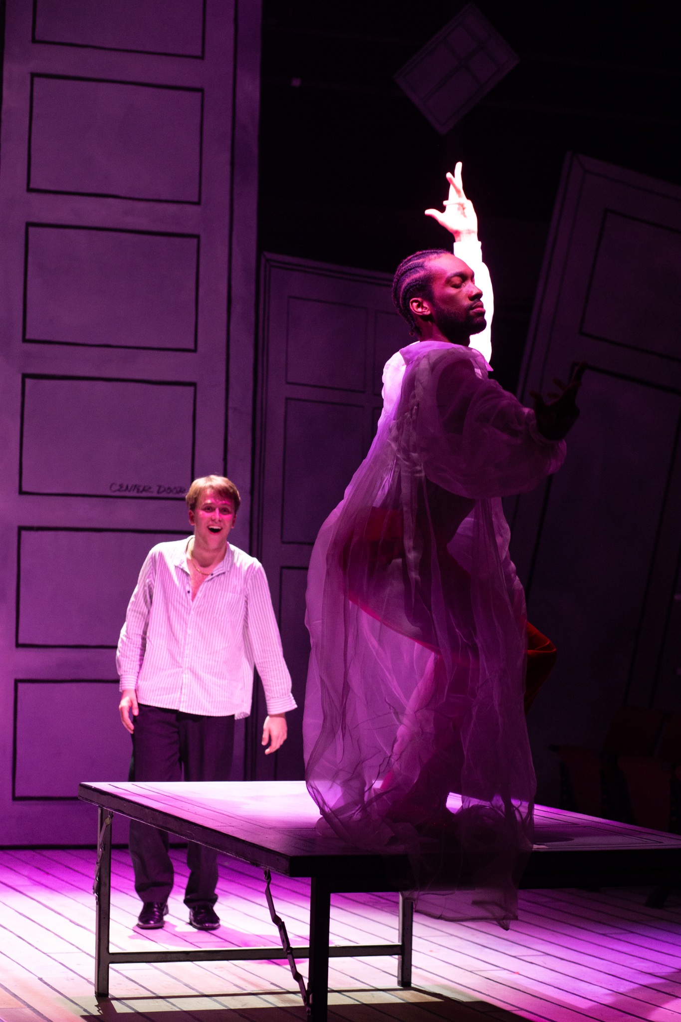 A performer reaches upward on a platform while another watches.